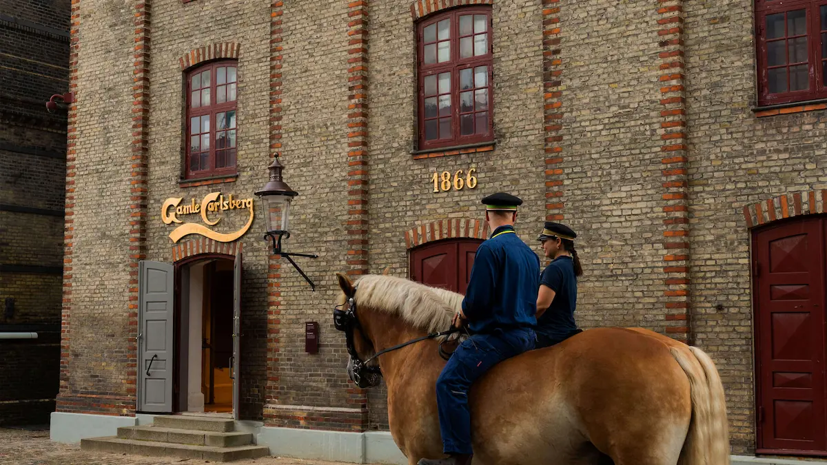 Ingresso della vecchia fabbrica Carlsberg a Copenaghen, con cavalli da tiro e insegna storica del 1866