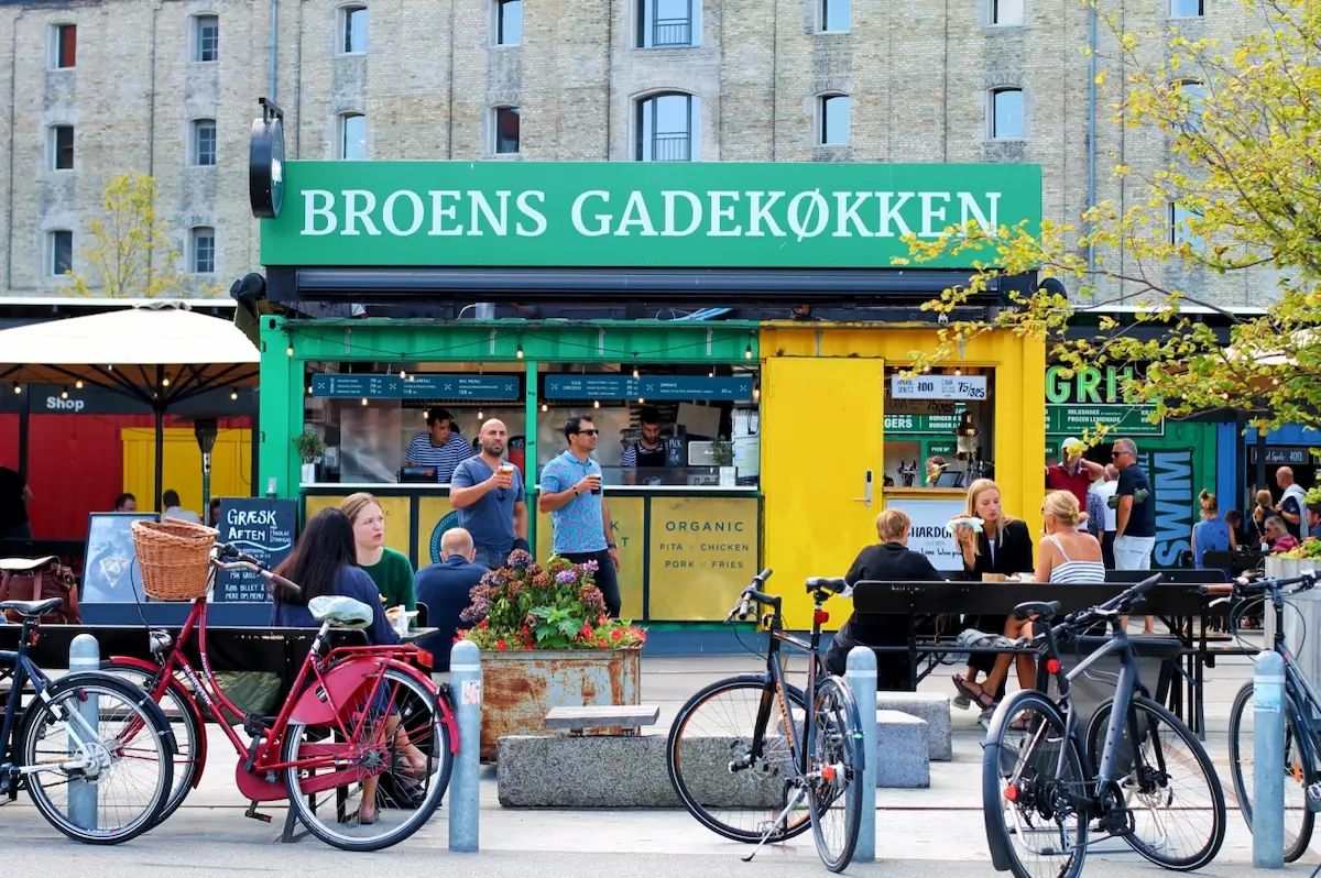 Broens Gadekøkken a Copenaghen, street food colorato sul porto con bici, gente seduta e atmosfera urbana.