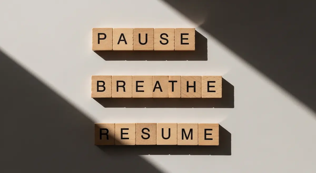 Tessere di legno con le parole “Pause, Breathe, Resume” illuminate dalla luce naturale.