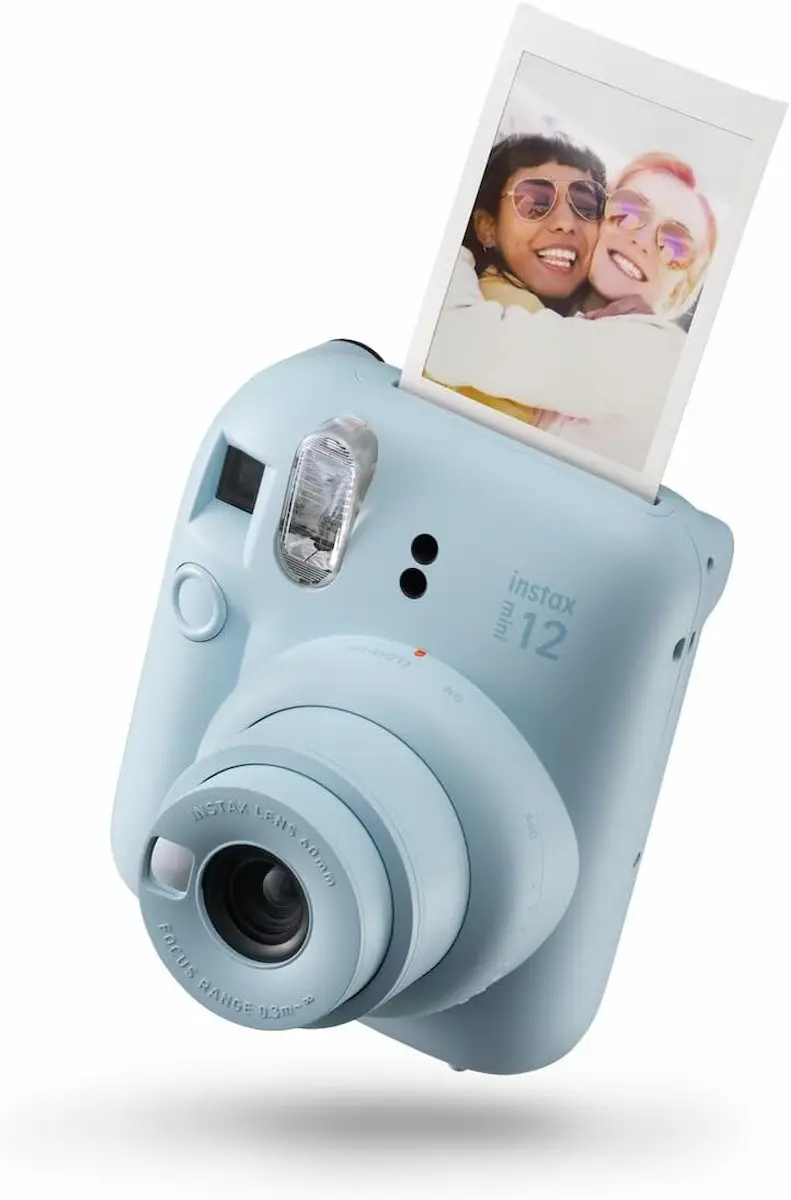 Fotocamera istantanea Instax Mini 12 azzurra che stampa una foto di due ragazze sorridenti. Regalo perfetto per teenager e creativi a Natale 2025