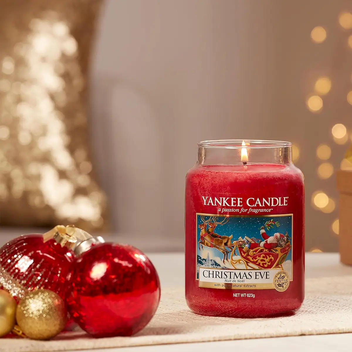 Candela rossa Yankee Candle Christmas Eve accesa su tavolo con decorazioni natalizie