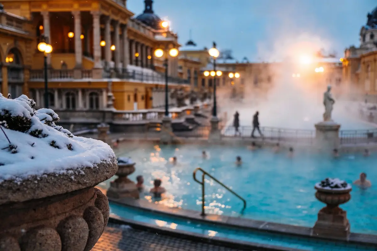 Terme all’aperto ispirate a Budapest in inverno con vapore, neve e architettura classica illuminata