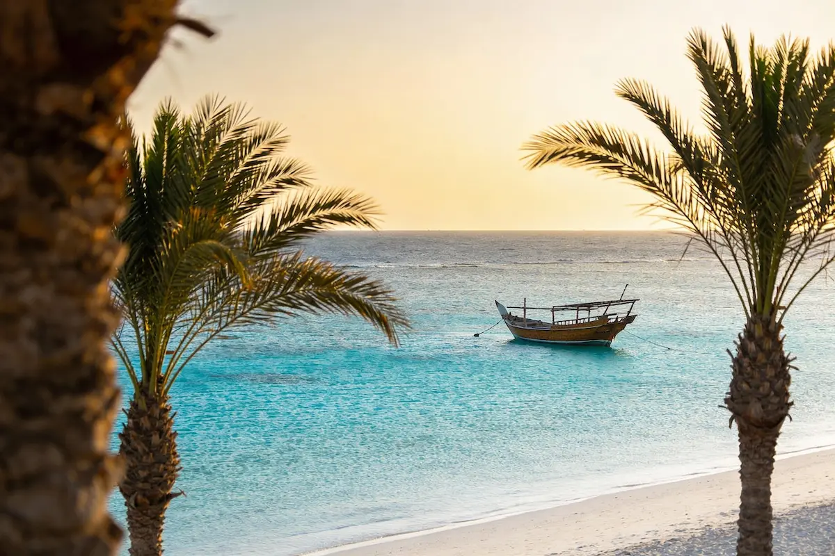 Mare turchese cristallino di Sharm el Sheikh al mattino presto con barca tradizionale ancorata e palme sulla spiaggia bianca