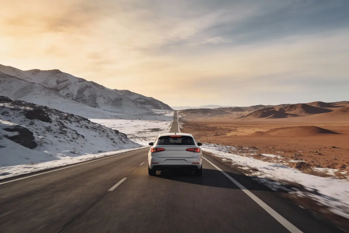 Auto chiara in viaggio su strada panoramica invernale tra montagne innevate e paesaggi aridi