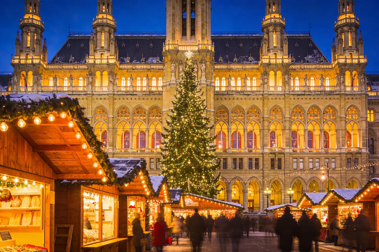 Mercatino di Natale a Rathausplatz a Vienna con casette di legno illuminate, grande albero decorato e Municipio sullo sfondo