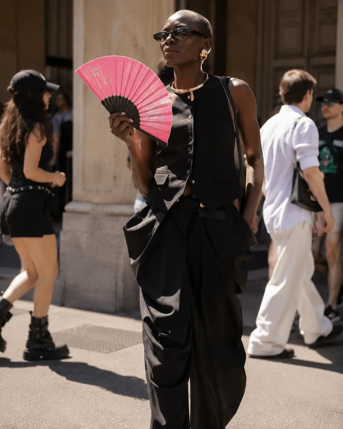 Donna in look nero con ventaglio rosa durante una scena street style dell’estate 2026.