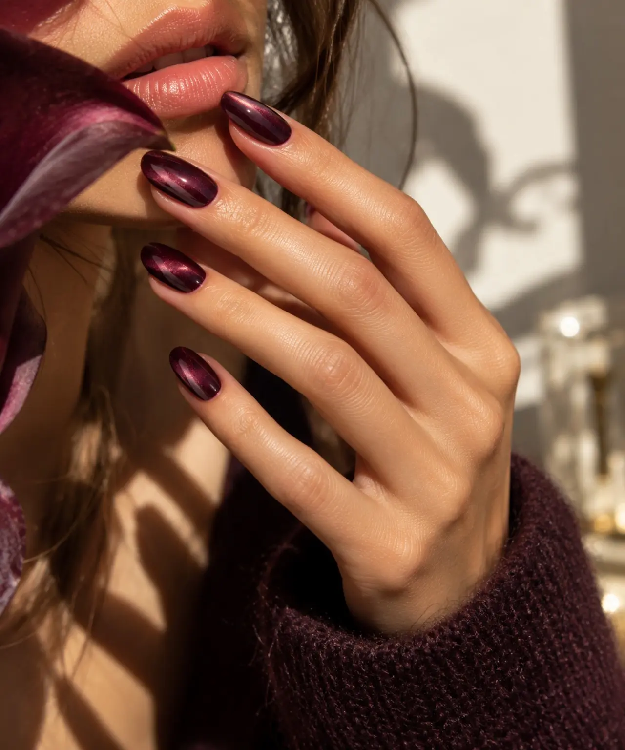 Mano in primo piano con Velvet Cat-Eye Nails borgogna e riflessi magnetici color prugna