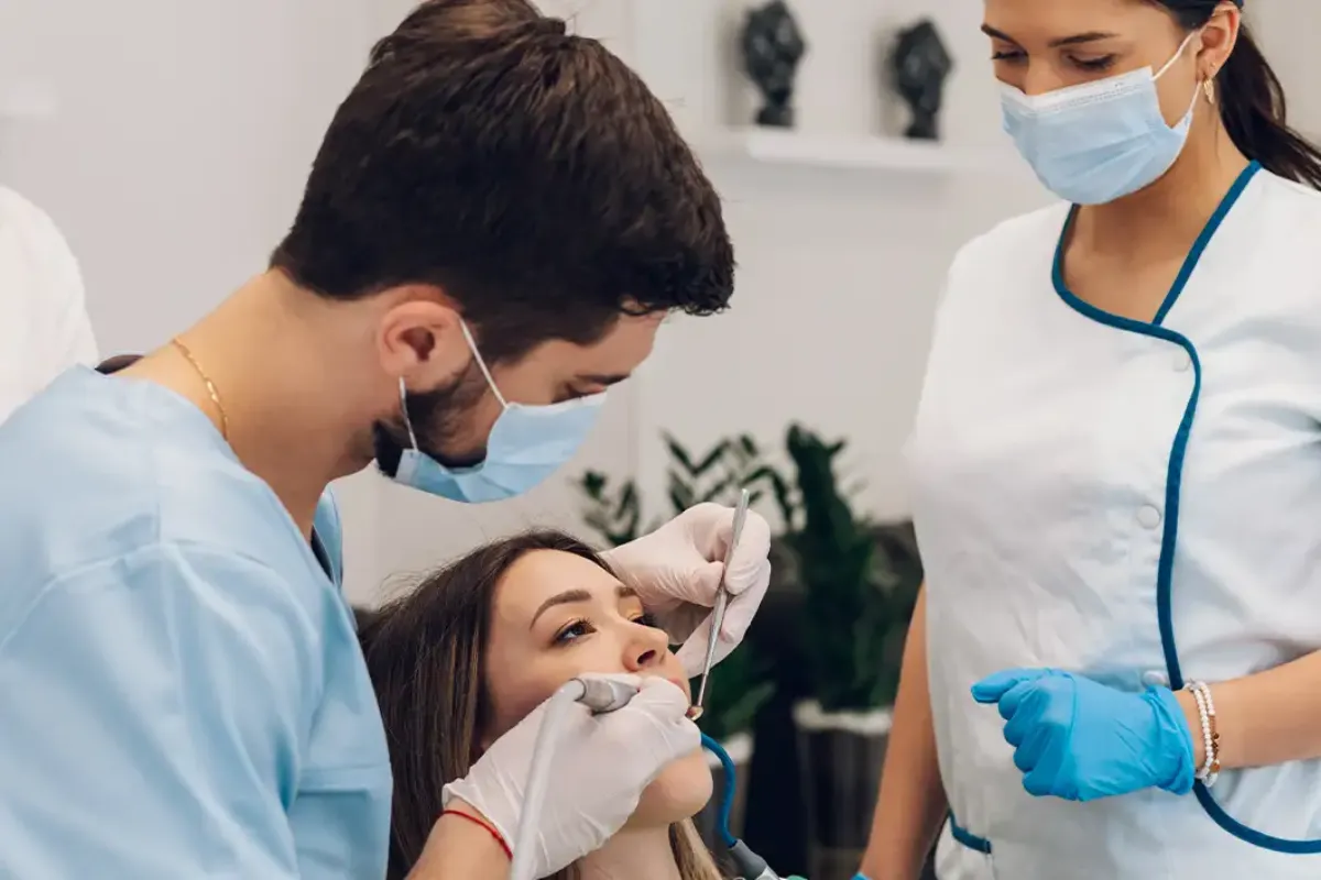 Faculdade de odontologia em BH com dentista e auxiliar atendendo paciente em consultório