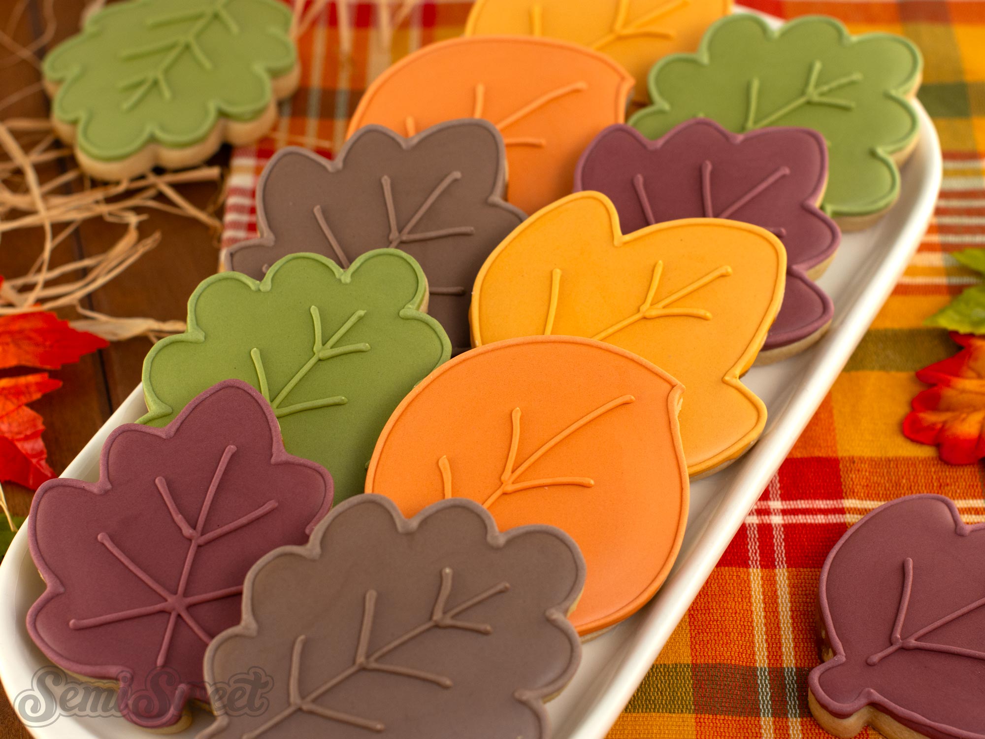 Fall leaf cookies decorated with orange, golden yellow, red, green, and brown royal icing arranged on a plate