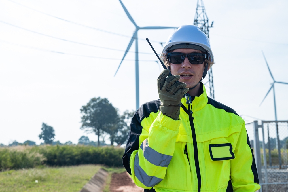 A wind site manager in protective equipment speaks into a radio 