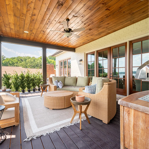 Covered outdoor patio with a wood-plank ceiling and ceiling fan, featuring wicker lounge seating, a round coffee table on a neutral rug, French doors, and an outdoor grill area.