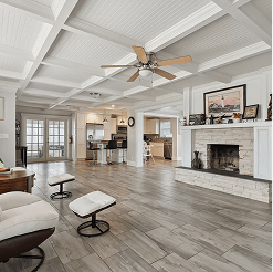 Open-concept living room and kitchen with a coffered white ceiling and ceiling fan, featuring a stone fireplace, tiled floors, and a modern kitchen with a breakfast bar.