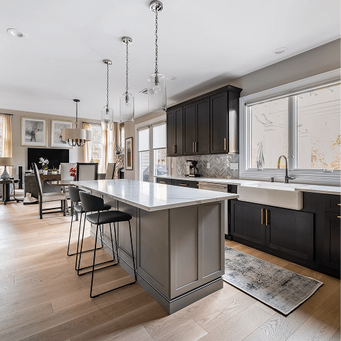 Modern open-concept kitchen with a large white quartz island, black cabinets, glass pendant lights, farmhouse sink, and bar stools, flowing into a bright dining area.