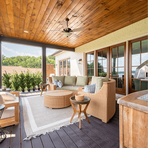 Covered outdoor deck with a wood ceiling and ceiling fan, featuring wicker patio seating, a round coffee table on an area rug, French doors, and a built-in grill station.