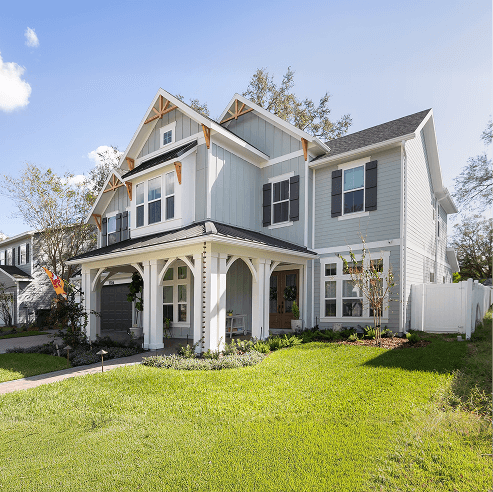Modern two-story farmhouse-style home with light gray siding, black shutters, and a covered front porch with white columns, set on a manicured green lawn.