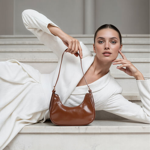 Woman in a white outfit posing on marble stairs with a brown leather shoulder bag in a fashion editorial portrait.