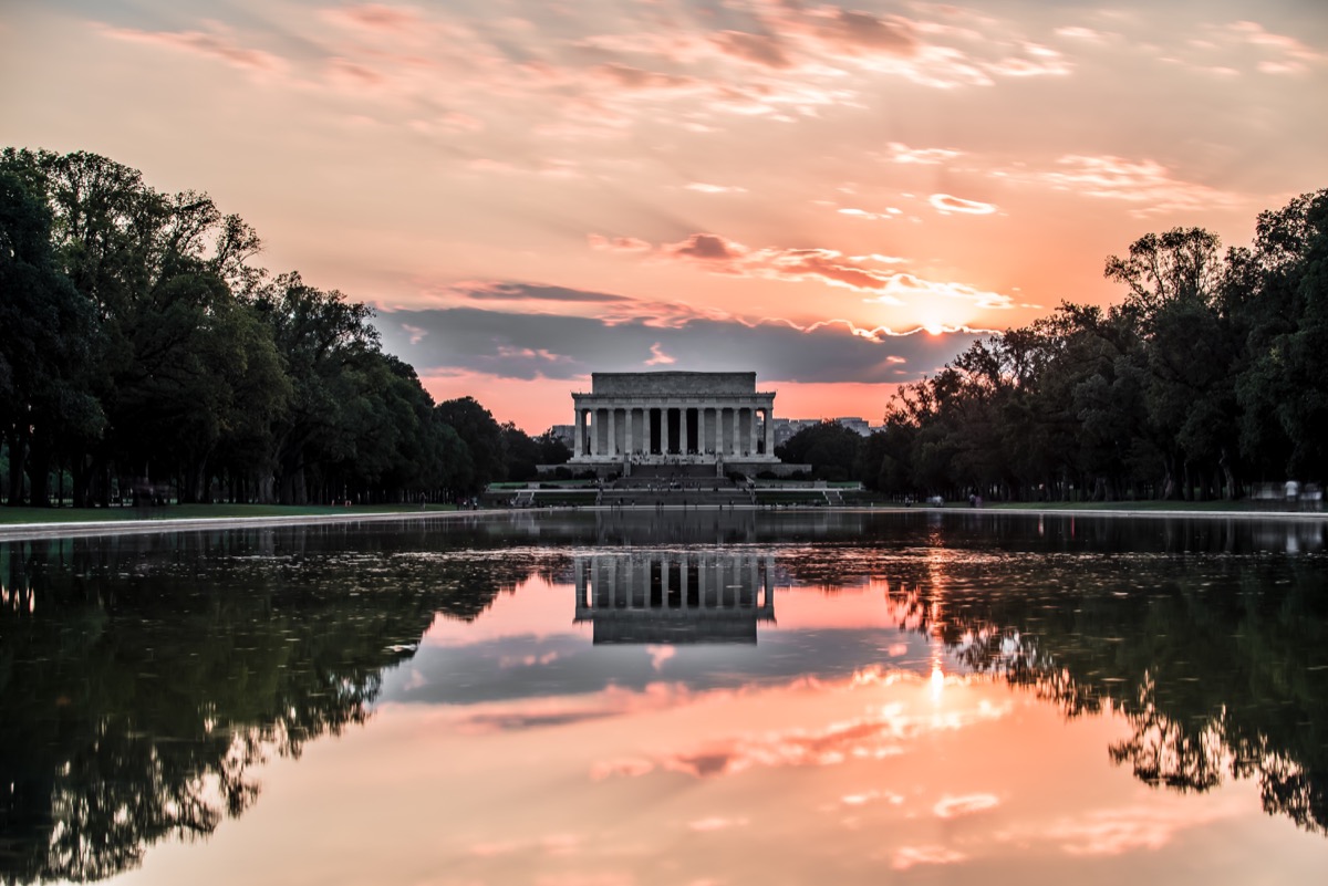 Lincoln Memorial in Washington DC at sunset reflected perfectly in the Reflecting Pool with pink and orange clouds overhead