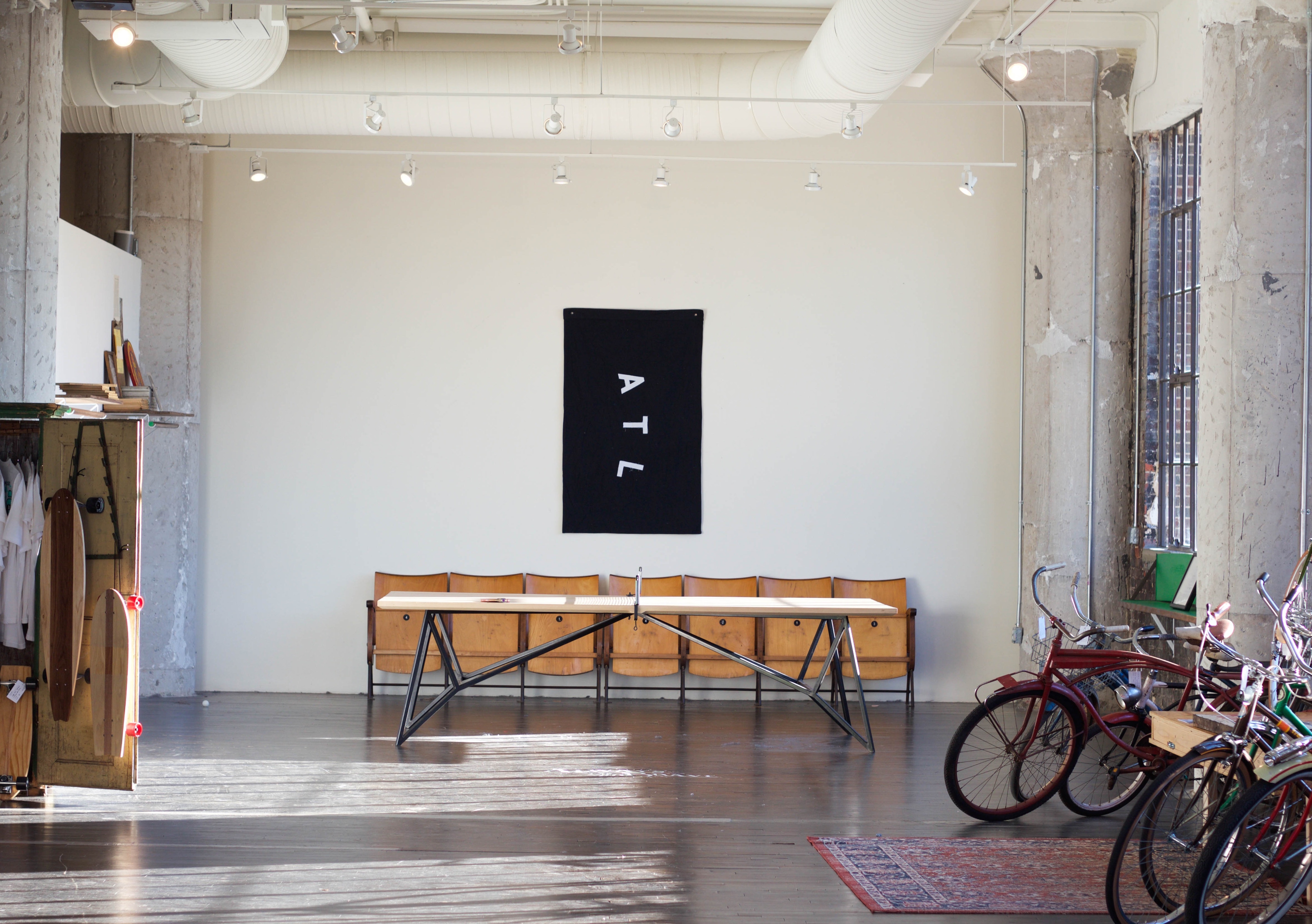 Industrial photography studio loft with exposed columns, vintage bicycles, wooden chairs as a bench, and a black ATL banner on the wall