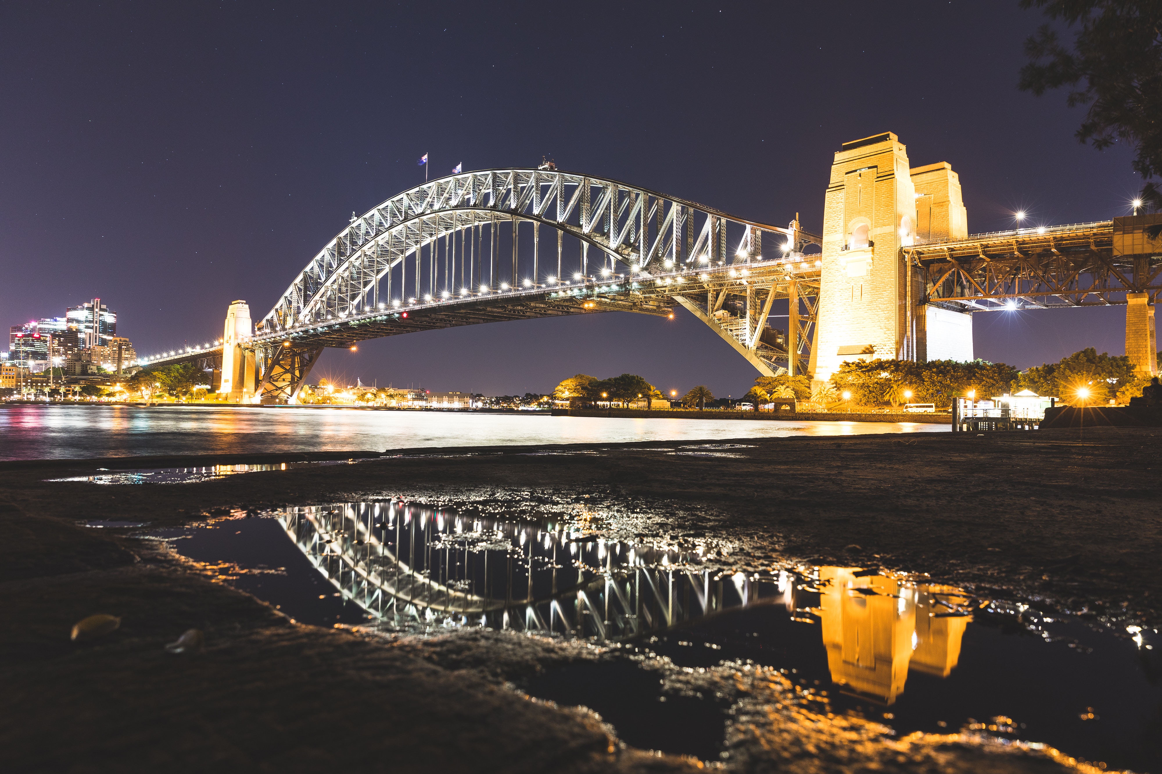 The Sydney Harbour Bridge illuminated at night with its lights reflected in a foreground puddle