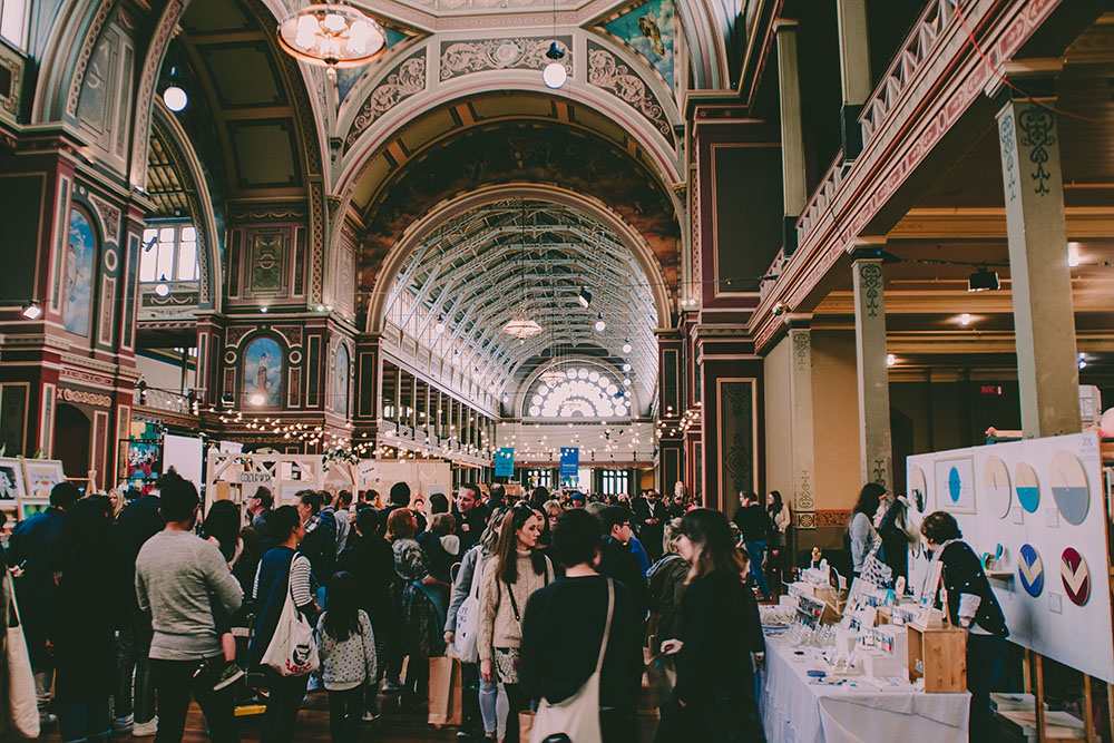 Interior of Melbourne's Royal Exhibition Building with a crowd attending a market under the ornate domed ceiling and arched windows