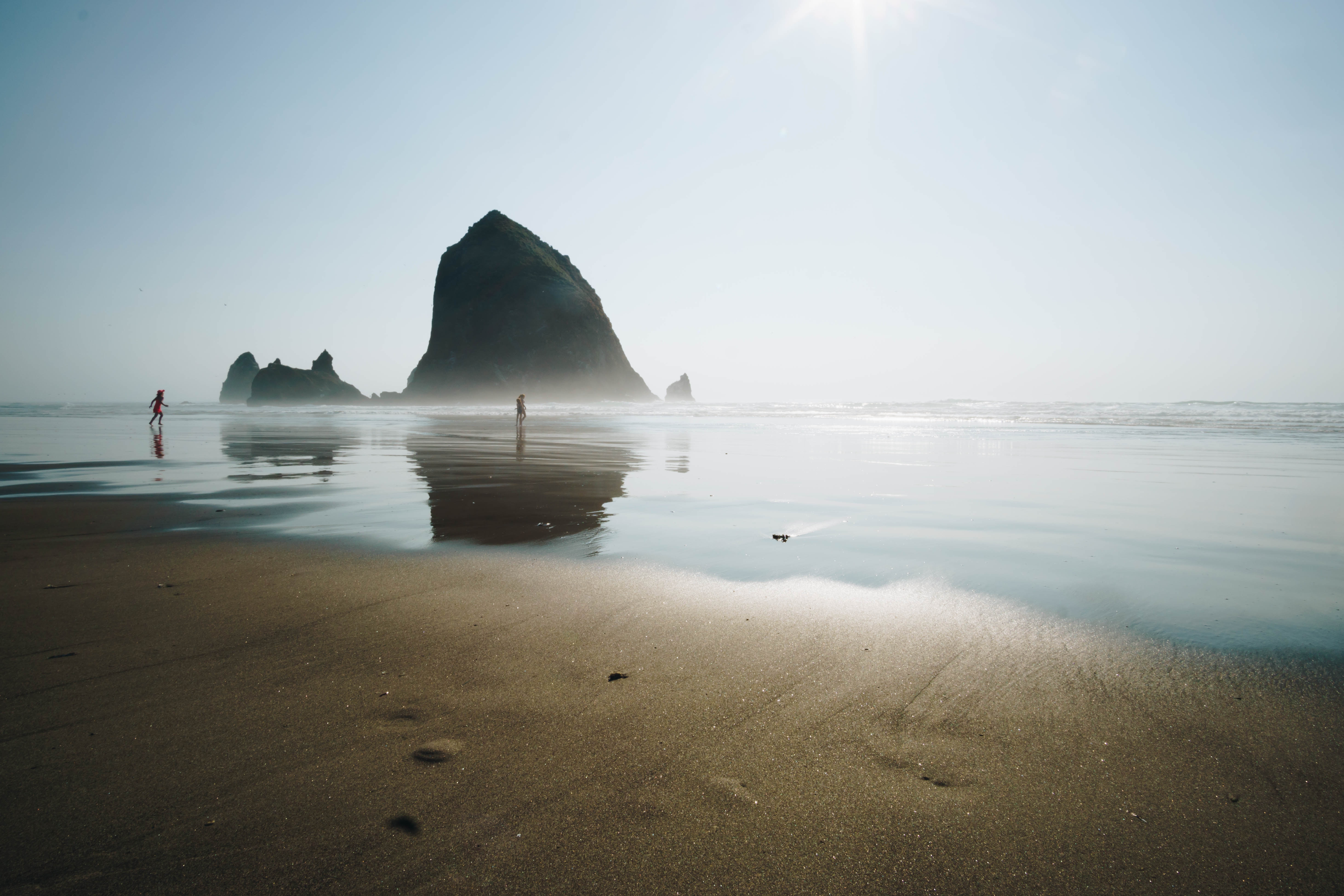 Haystack Rock and the Needles sea stacks at Cannon Beach Oregon with people walking on wet reflective sand