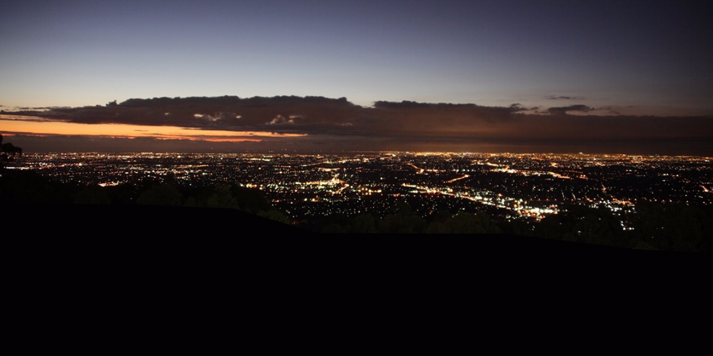 Panoramic view of city lights at twilight from a hilltop overlook with a faint orange band on the horizon