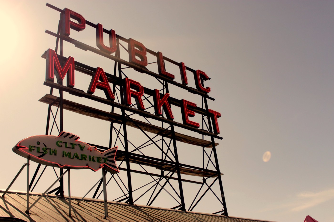 Pike Place Public Market neon sign and City Fish Market sign at sunset with the moon visible in Seattle
