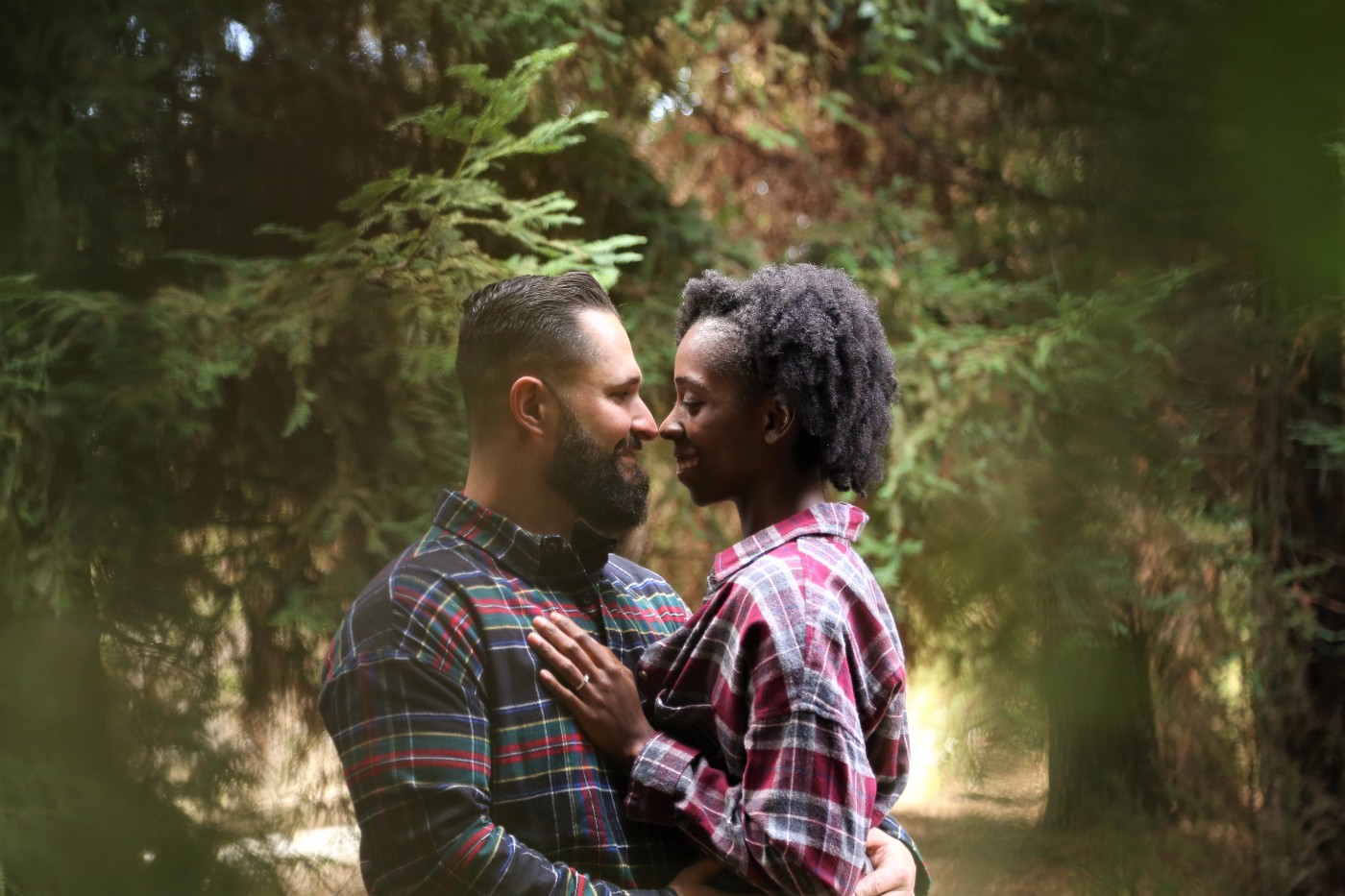 Engaged couple in plaid shirts standing in a forest with foreheads touching for an intimate engagement portrait