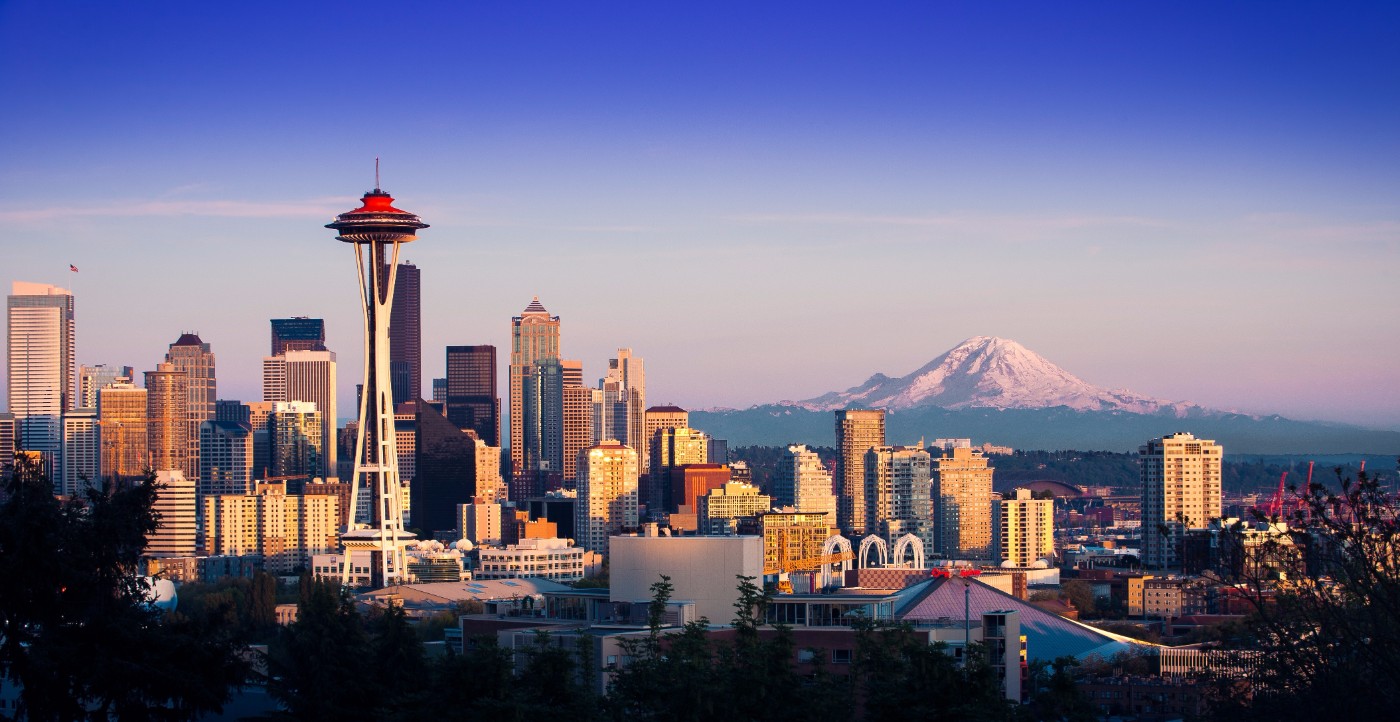Seattle skyline at dusk with the Space Needle on the left and snow-capped Mount Rainier rising behind the downtown skyscrapers