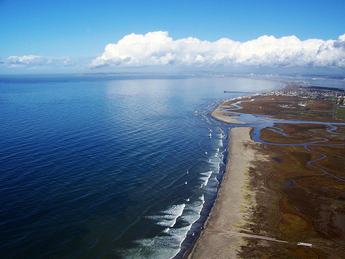 Aerial view of the Tijuana River Estuary coastline with crashing ocean waves, sandy beach, and meandering river channels