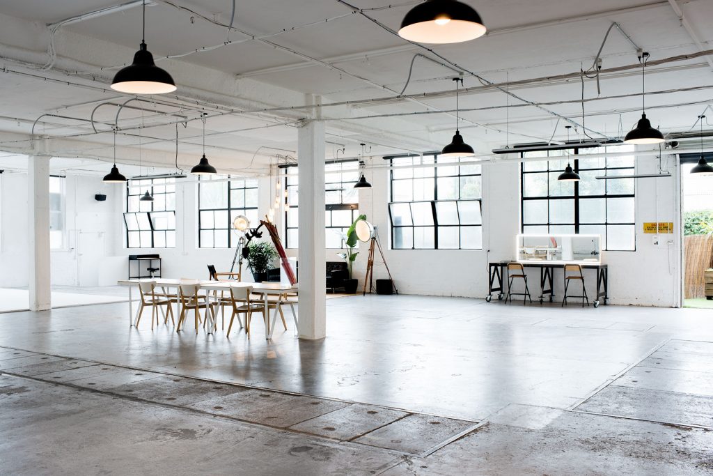 Spacious open-plan photography studio interior with industrial pendant lights, white columns, polished concrete floor, and large factory windows
