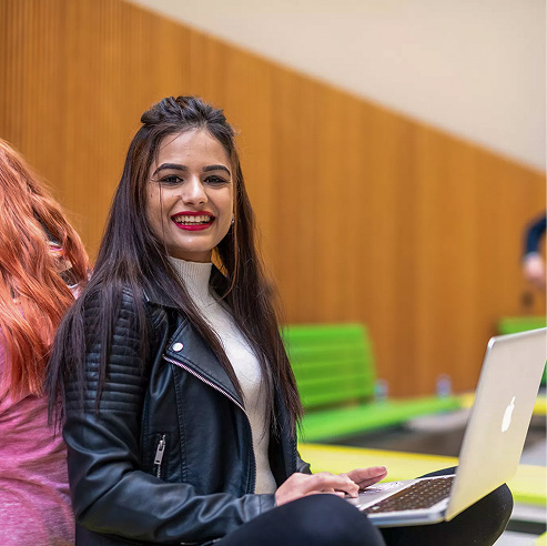 Young woman smiling at her laptop while networking at a professional business event.
