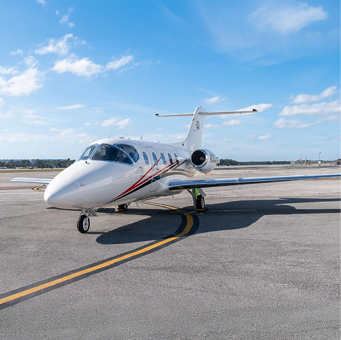 White private jet parked on a sunlit tarmac at an airport with a clear blue sky.