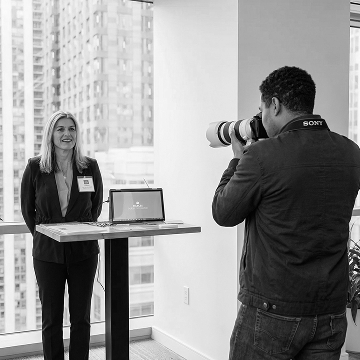 Photographer setup capturing a woman speaker at a conference exhibition booth.