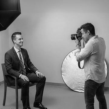Photographer using a reflector to shoot a seated man in a studio portrait session