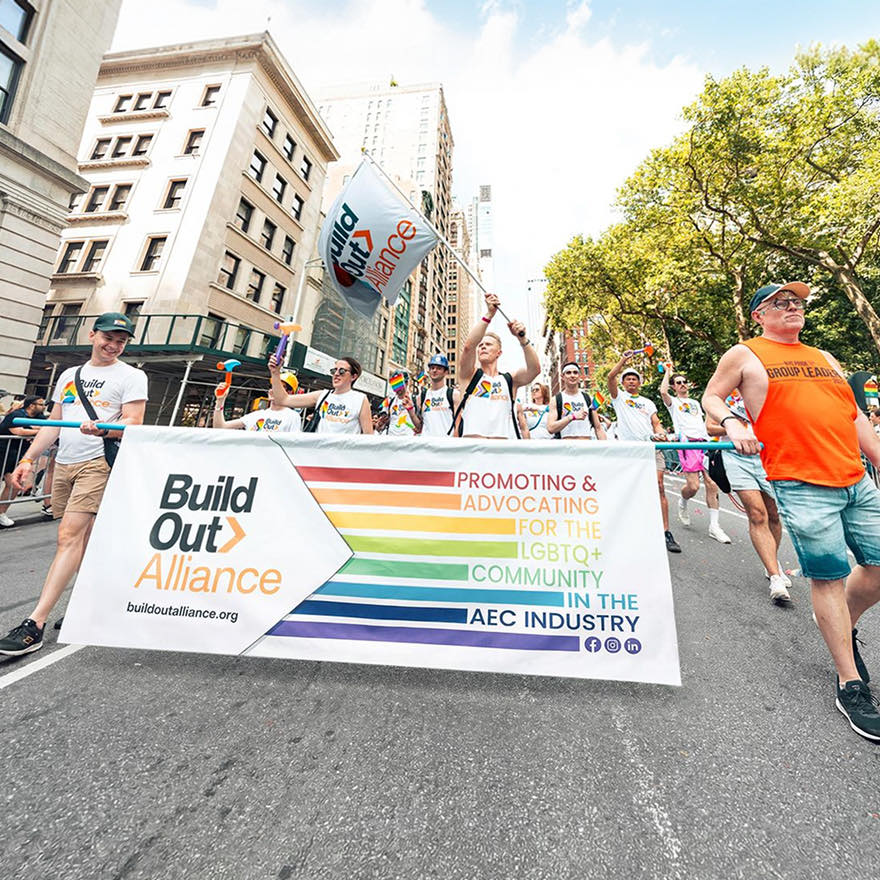 LGBTQ Pride parade marchers carrying a Build Out Alliance banner down a city street.