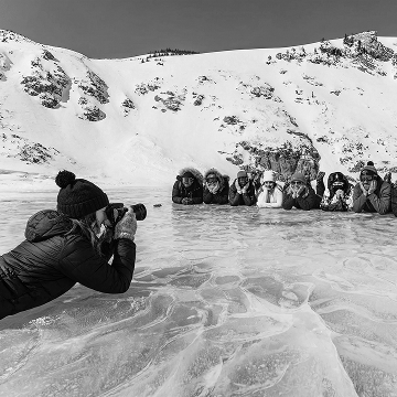 Photographer and crew setting up a winter group shoot on a frozen lake with snowy mountains.