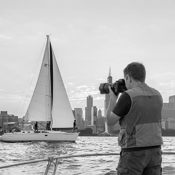 Photographer on a boat capturing a sailboat with the Chicago city skyline in the background.