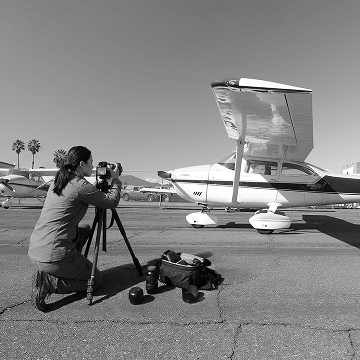 Photographer on a tripod at an airport capturing a small aircraft for an aviation photoshoot.