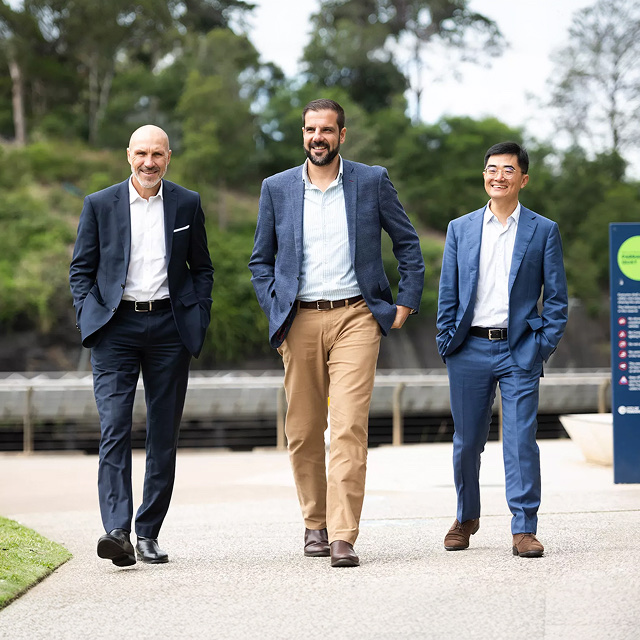 Three businessmen in suits walking together across an outdoor corporate campus area.