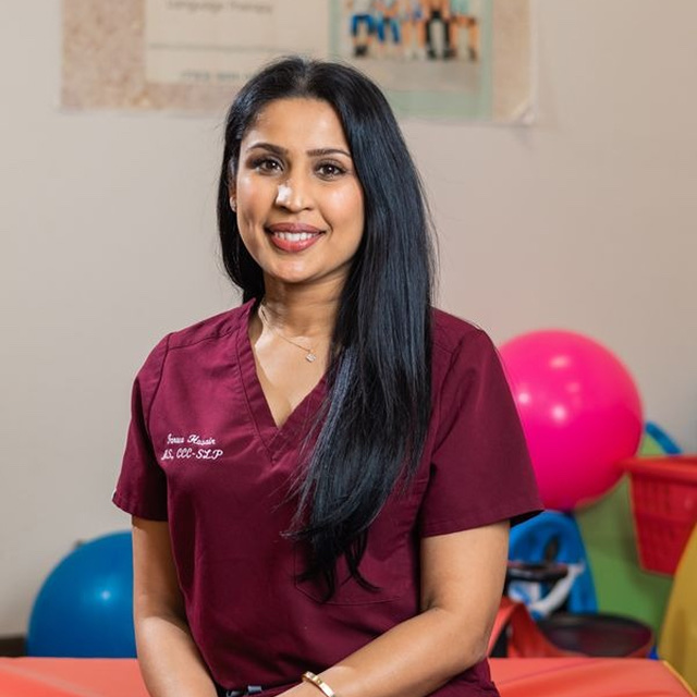 Female healthcare worker in maroon scrubs posing for a professional portrait at a clinic.