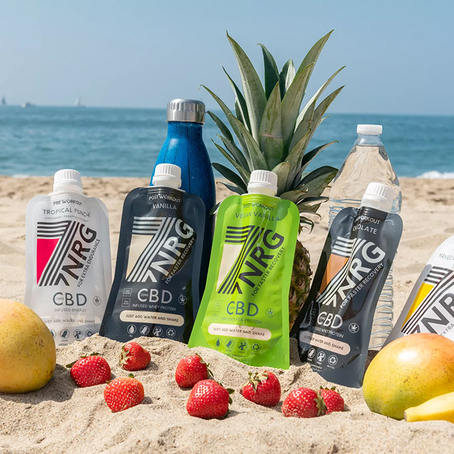 7NRG CBD protein pouches arranged on beach sand surrounded by tropical fruit for a lifestyle ad.
