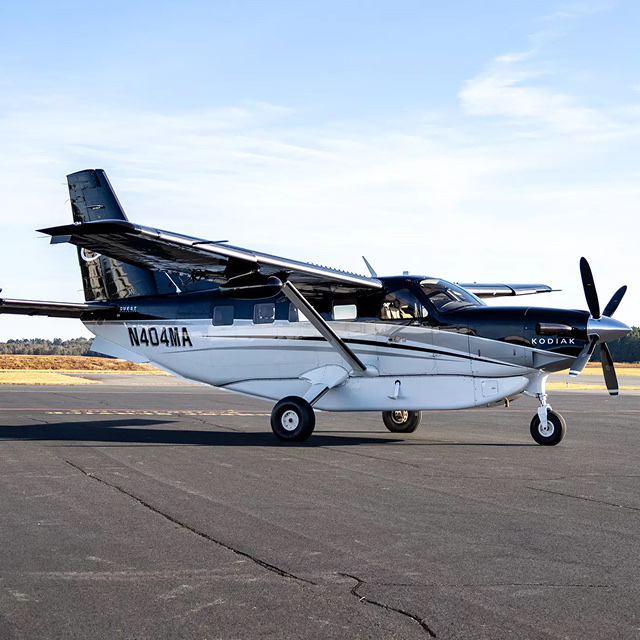 Kodiak turboprop aircraft parked on a tarmac at a small regional airport.