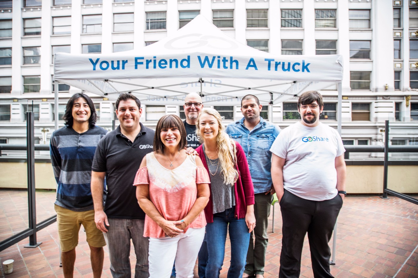 GoShare team group photo of seven members posing under Your Friend With A Truck branded canopy on rooftop