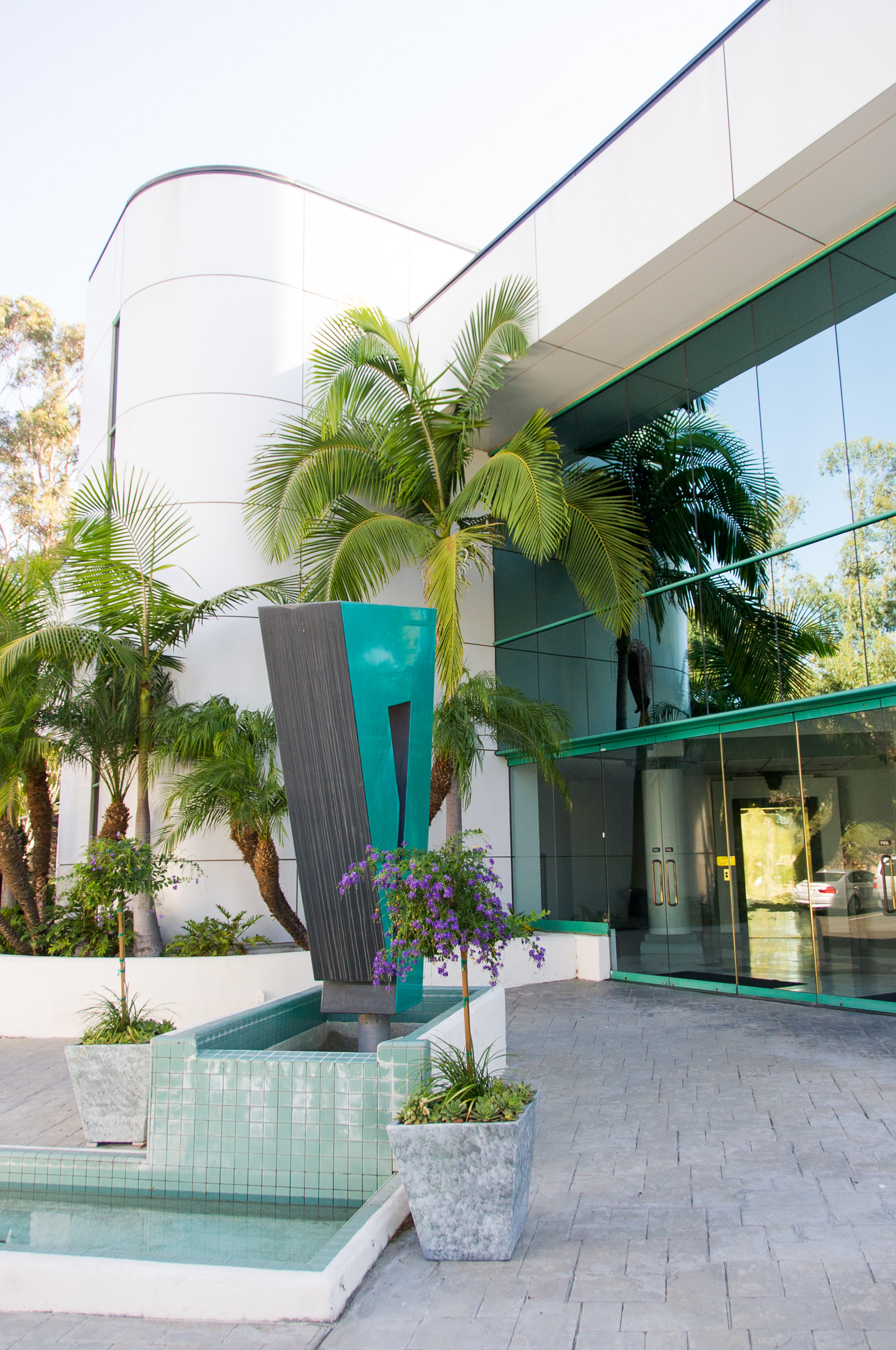 Modern Lawn Love office building exterior with palm trees, geometric sculpture, fountain, and reflective glass entrance