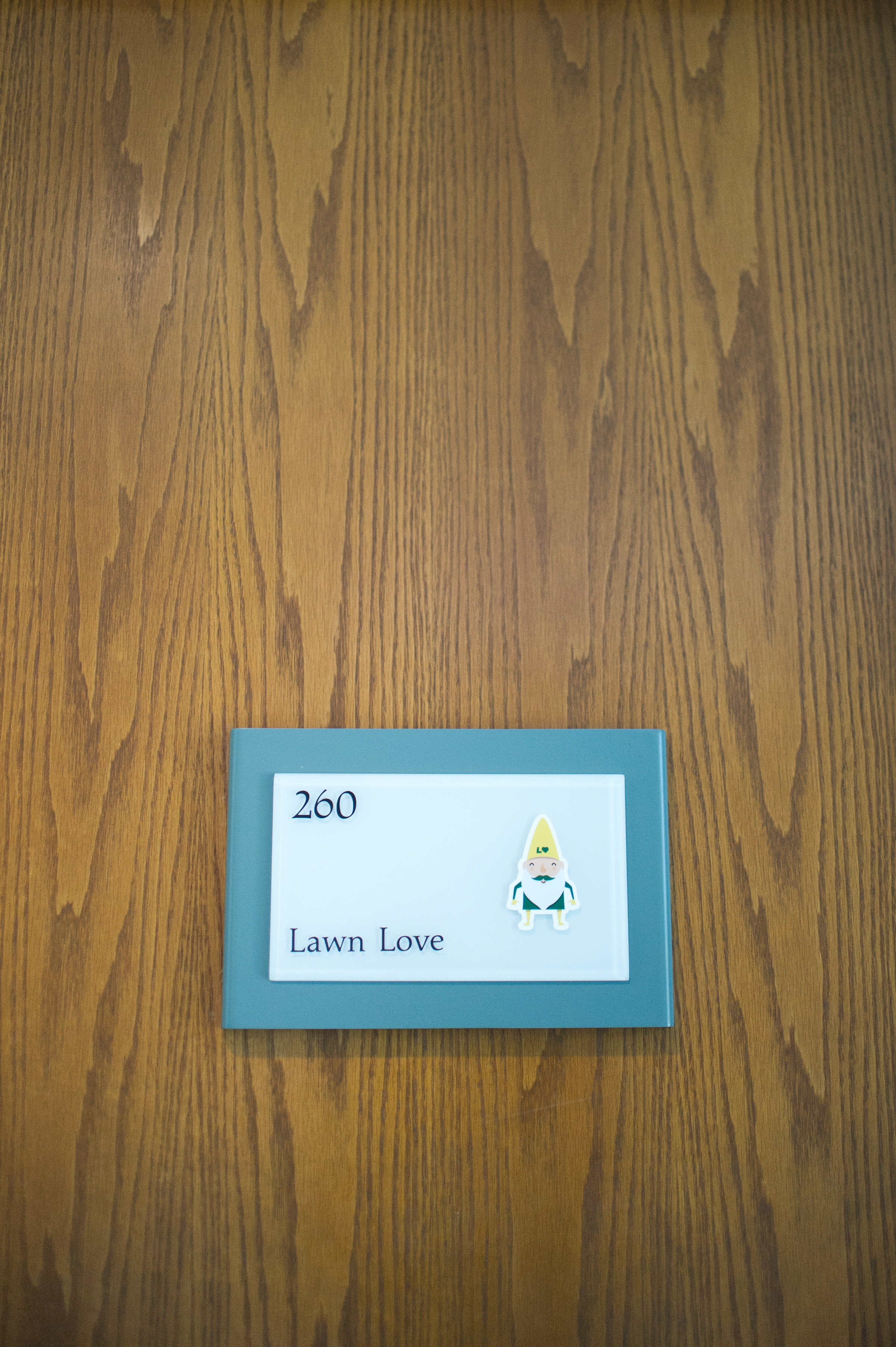 Wooden door with Lawn Love office sign showing suite number 260 and gnome mascot logo