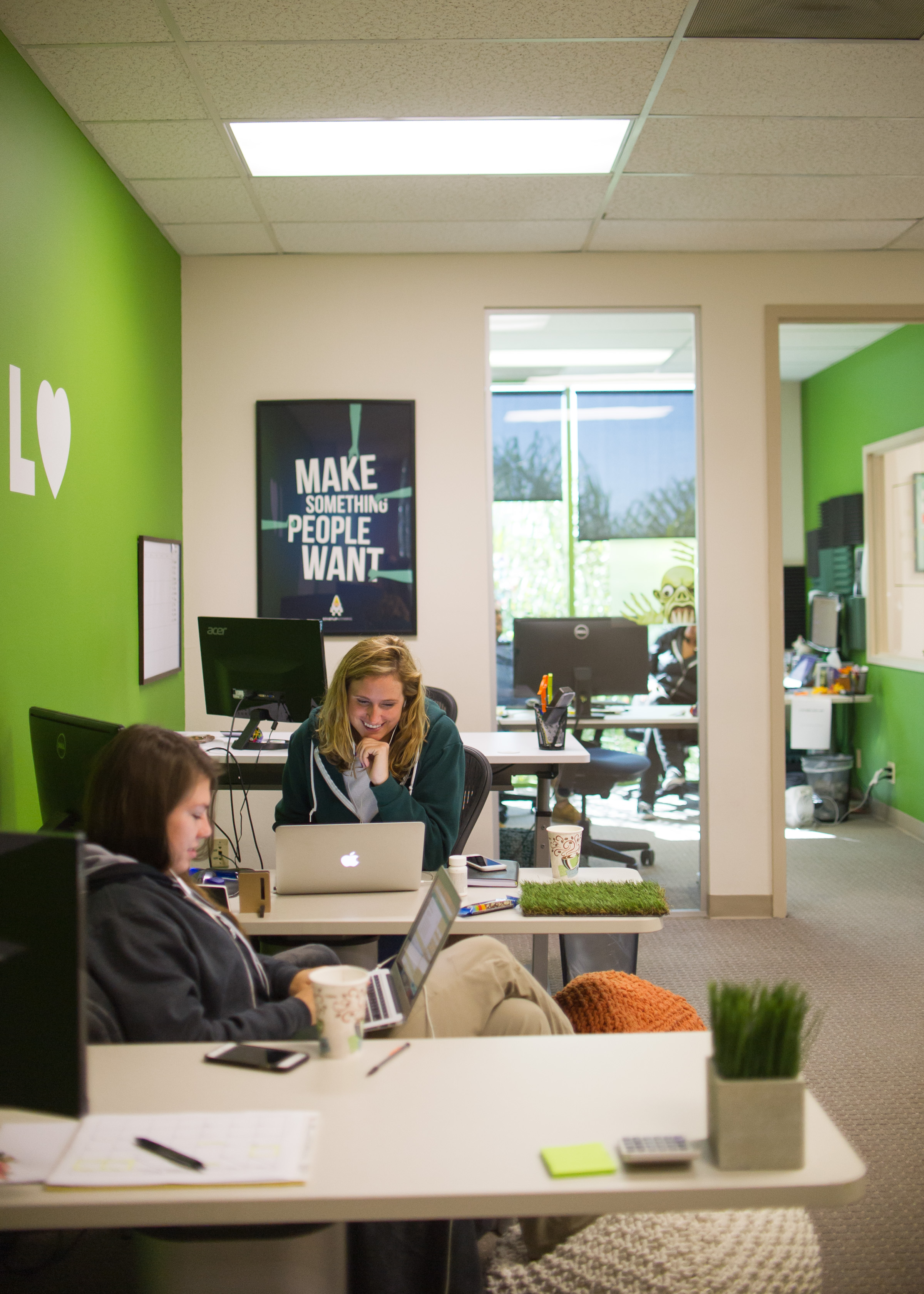 Lawn Love office interior with team members working at desks, green accent walls, and Make Something People Want poster