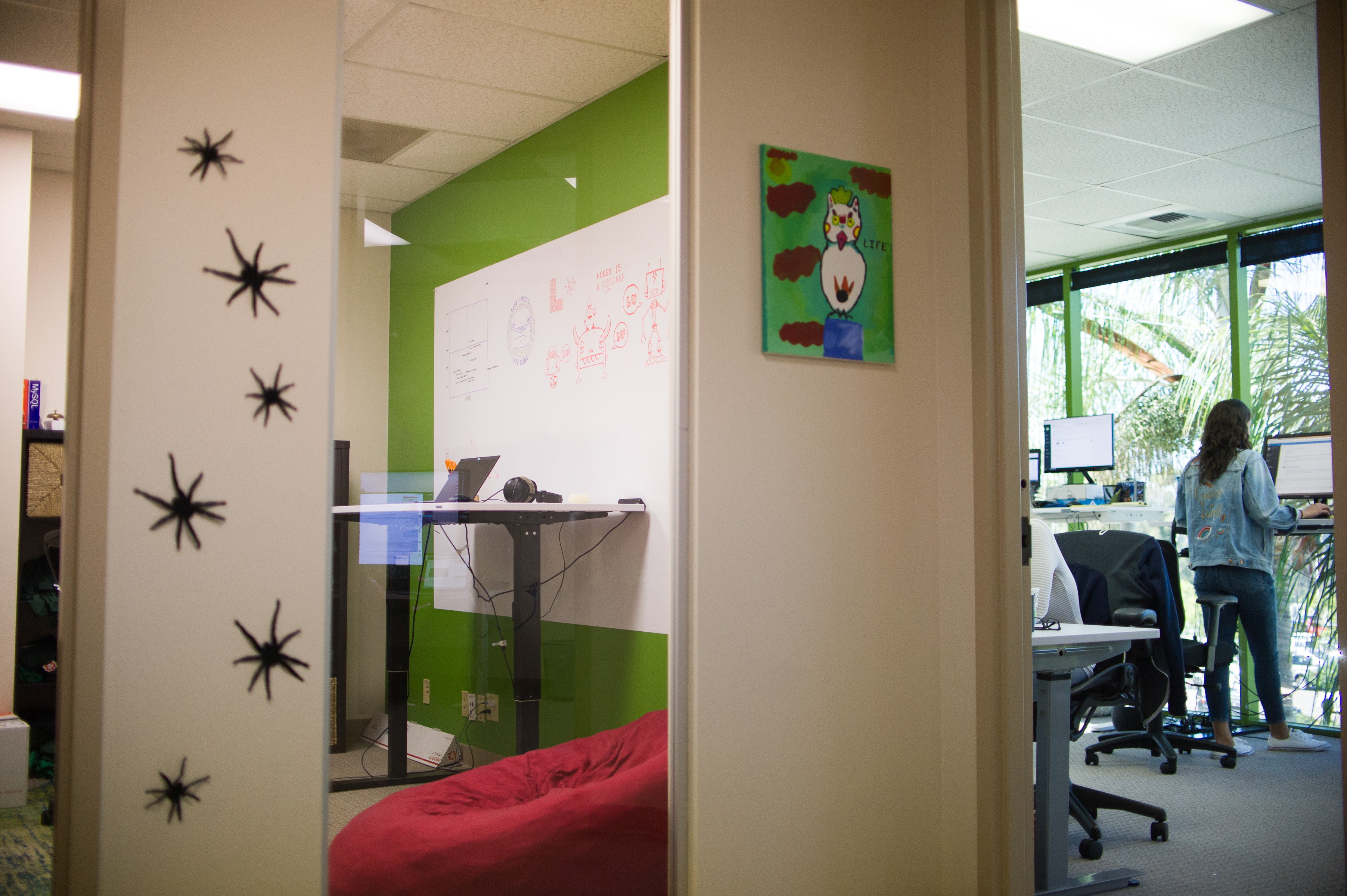 Lawn Love office interior with green accent walls, whiteboard, child's artwork on wall, and team member working at standing desk