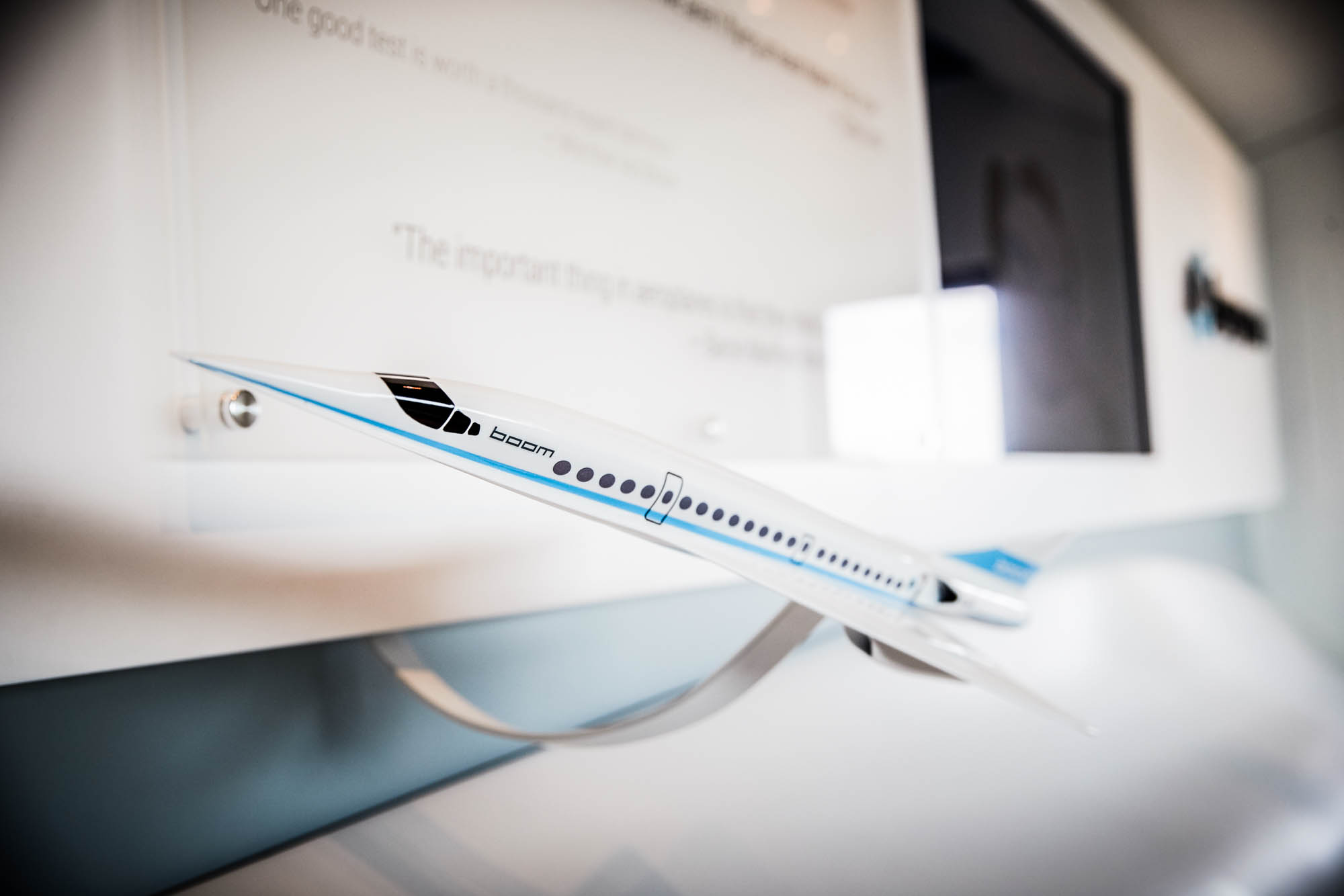 Close-up of a Boom Overture supersonic airliner scale model on display with company logo and inspirational quote signage in the background
