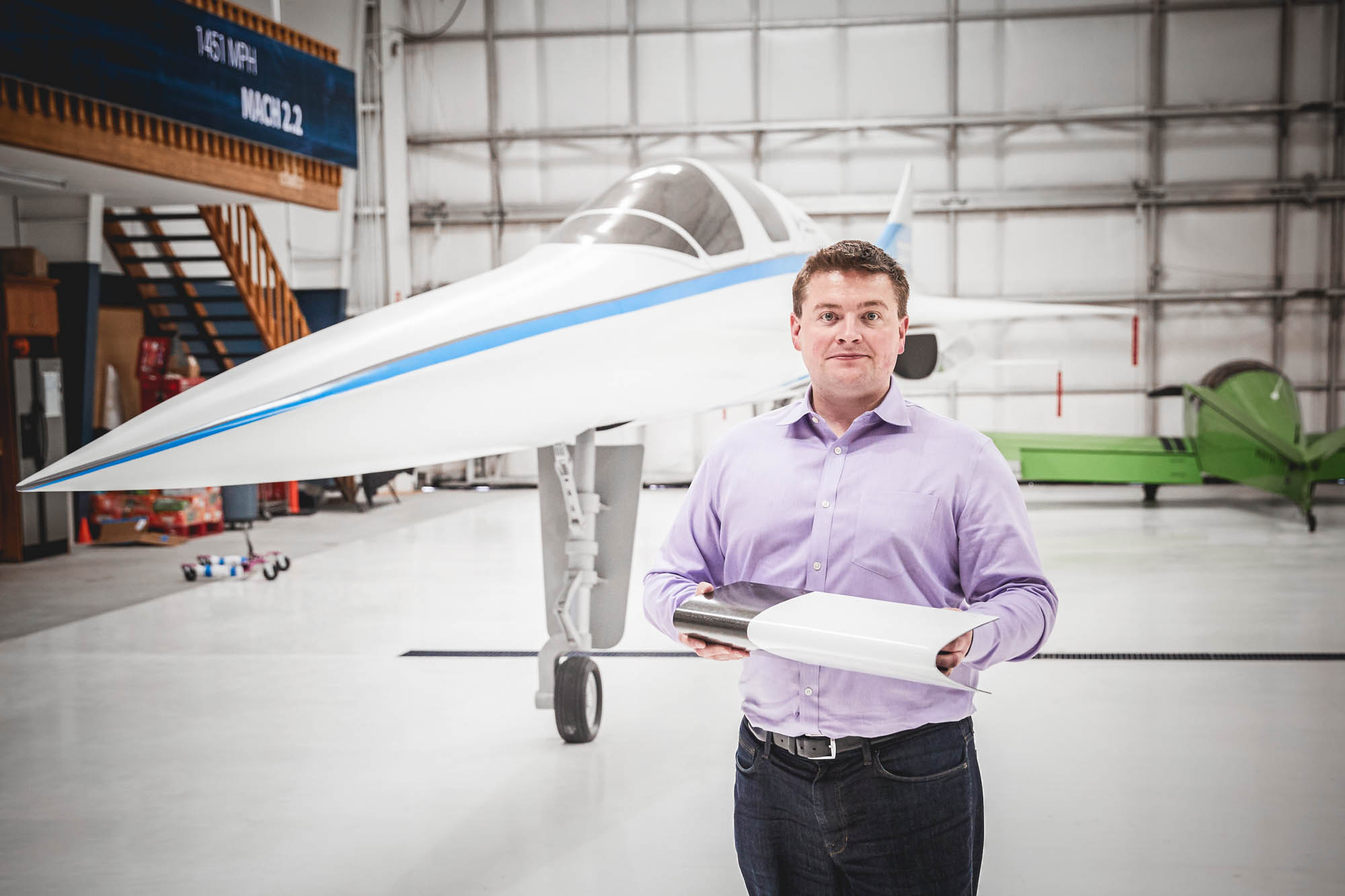 Boom Supersonic CEO Blake Scholl holding aircraft components in front of XB-1 supersonic jet prototype in hangar